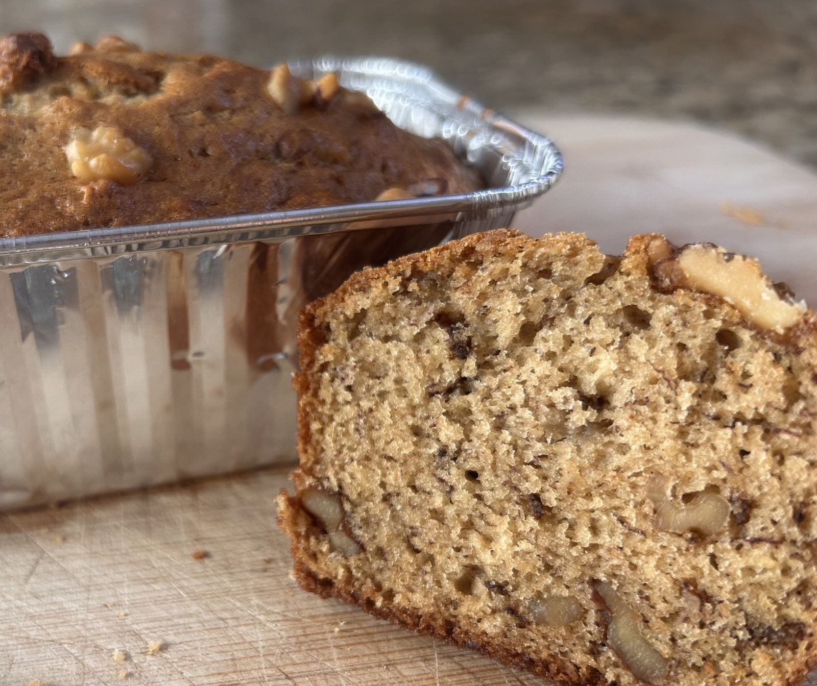 walnut bourbon banana bread in a mini loaf pan and a piece is cut with a bottle of bourbon in the background