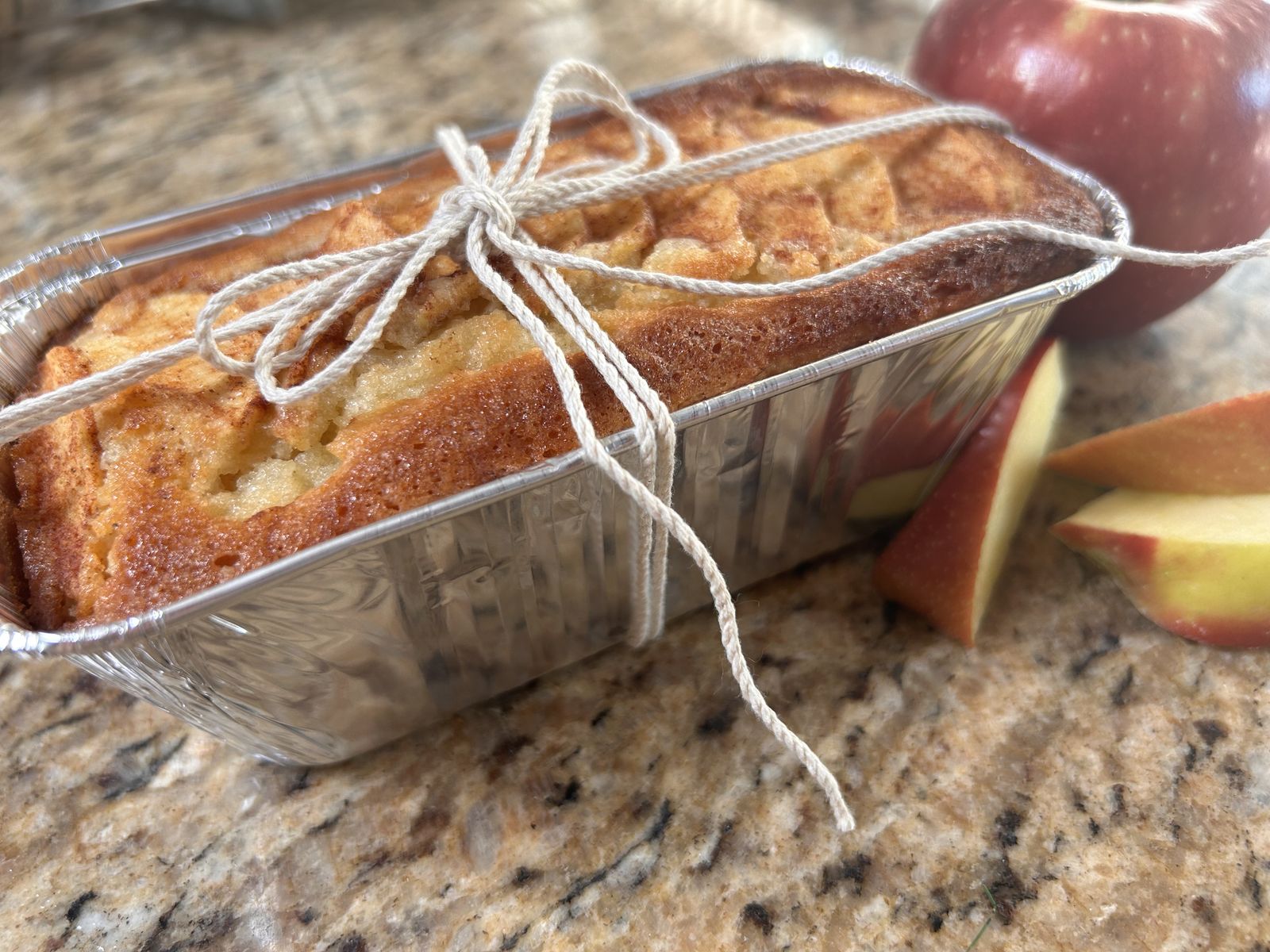 sweet apple cake in a mini pan with a twine bow around it in a whole and cut up apples next to the pan
