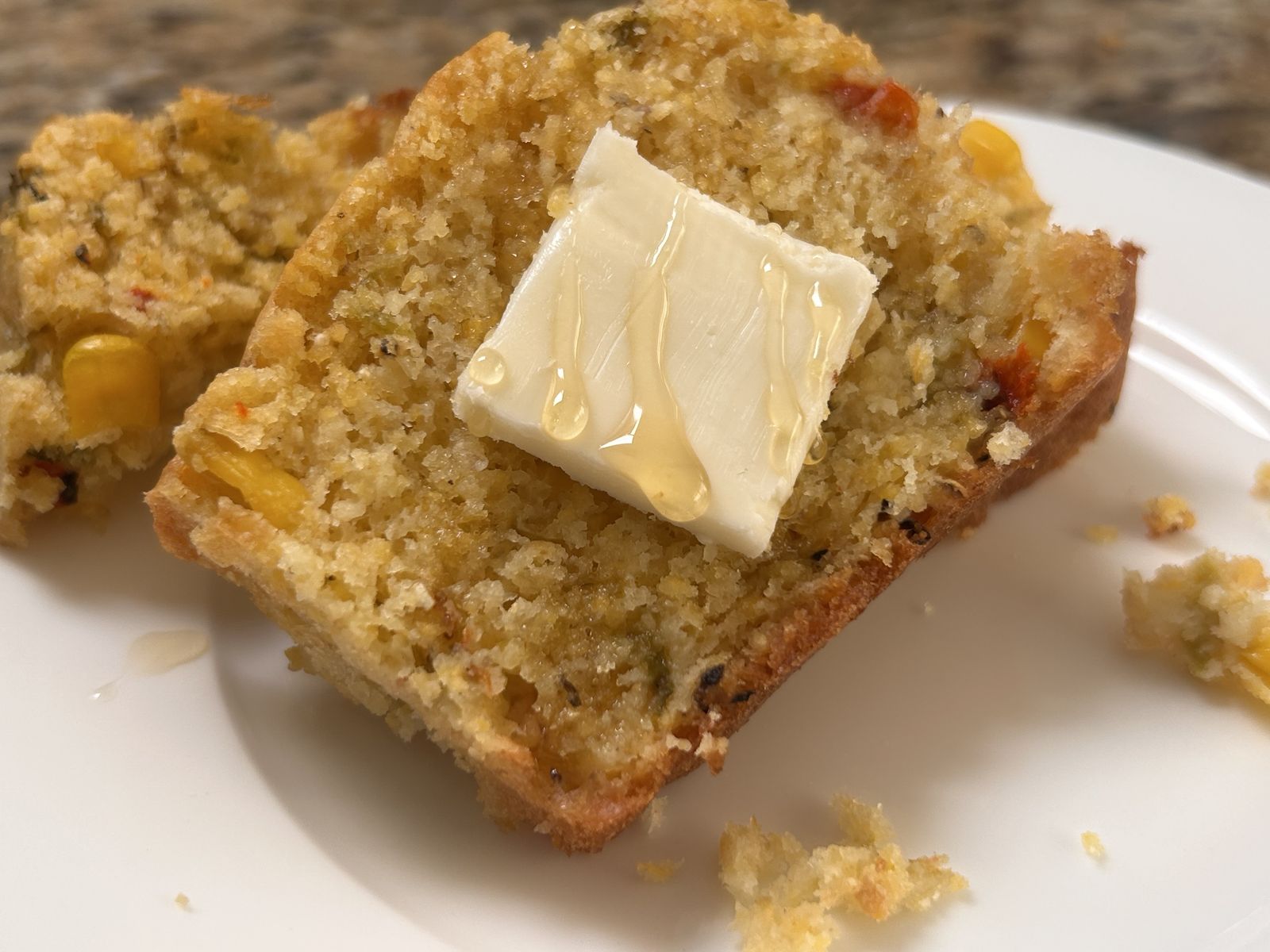 a slice of green chile corn bread topped with a pat of butter and a drizzle of honey